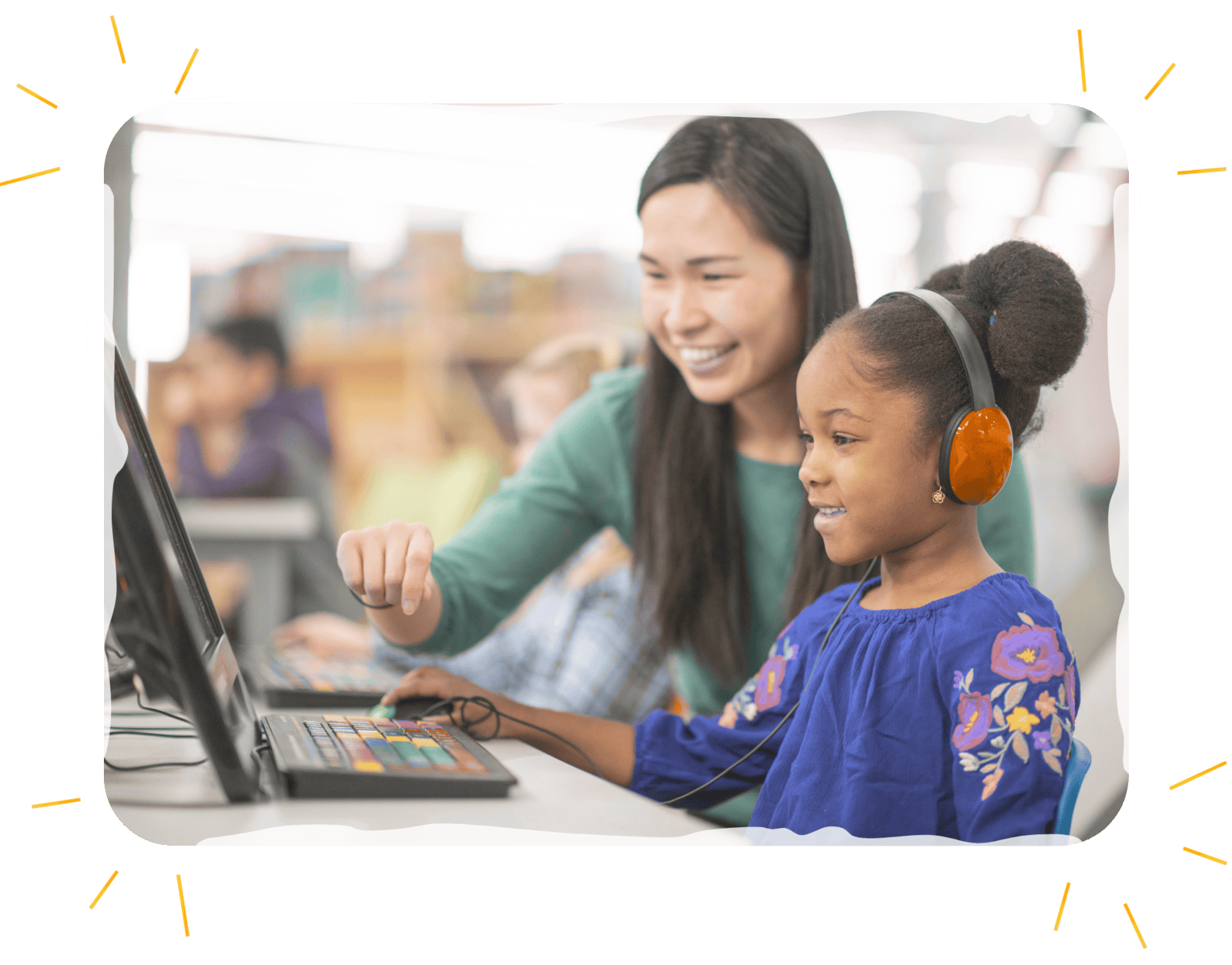 Teacher guiding elemenary aged student through computer program with headphones